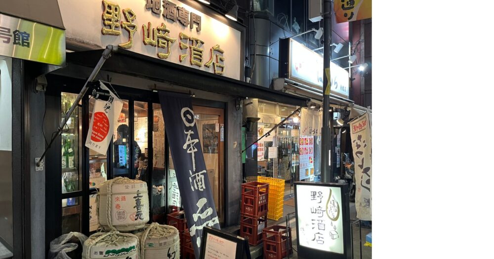 新橋の野崎酒店の外観。夜の街角で日本酒を楽しむ酒場の雰囲気を伝える